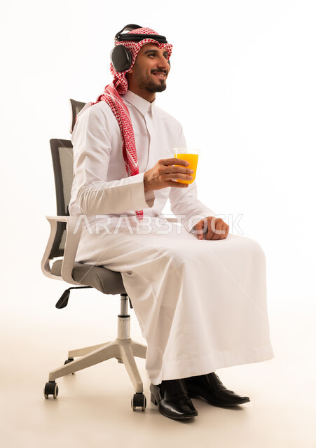 رجل سعودي يرتدي سماعات ويشرب العصير على كرسي مكتب