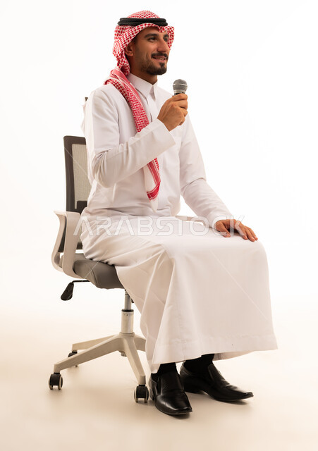 رجل سعودي يحمل ميكروفون على كرسي مكتب بخلفية بيضاء