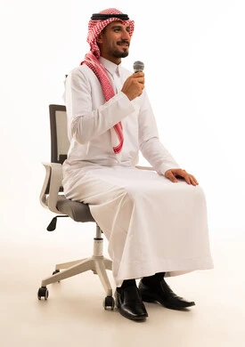رجل سعودي يحمل ميكروفون على كرسي مكتب بخلفية بيضاء