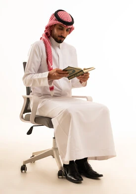رجل سعودي بالثوب التقليدي يقرأ القرآن الكريم