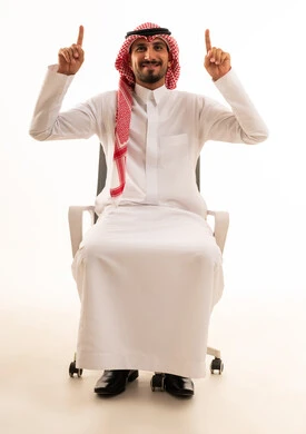 رجل سعودي بالزي التقليدي يشير للأعلى على كرسي