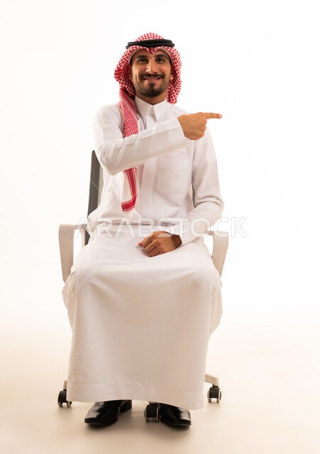 رجل سعودي بالزي التقليدي يشير بيده على كرسي مكتب