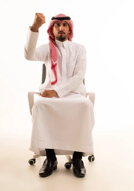 Saudi Man in Traditional Dress Raising Fist on Chair