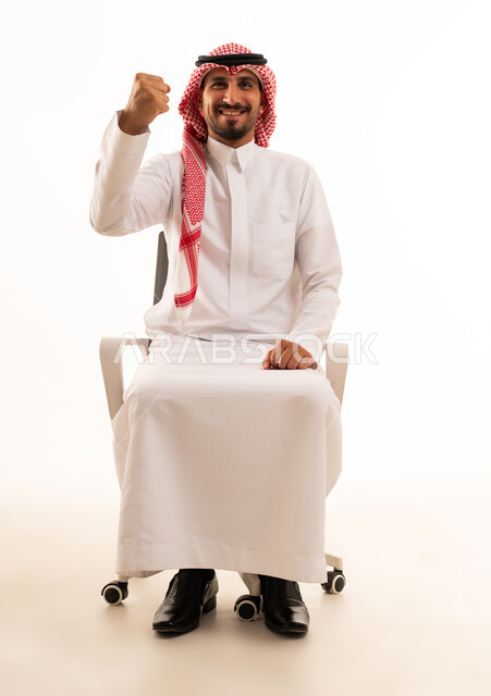 رجل سعودي بالزي التقليدي يرفع قبضة يده تعبيراً عن النجاح