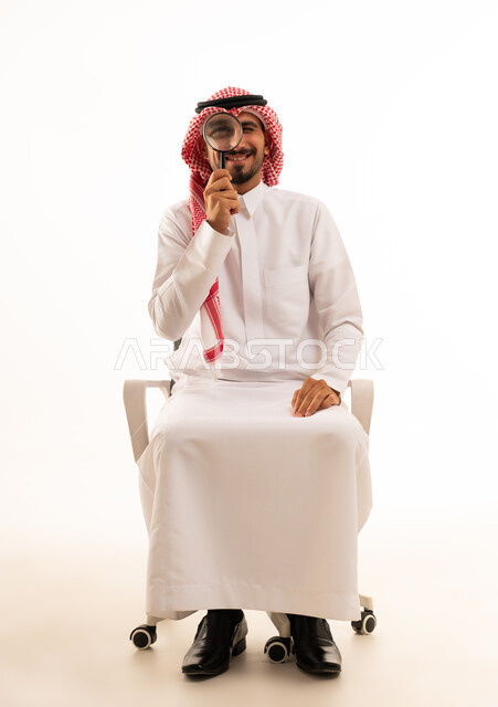 رجل سعودي يحمل عدسة مكبرة على خلفية بيضاء