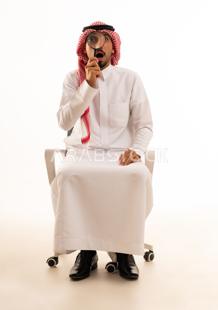 رجل سعودي يحمل عدسة مكبرة على خلفية بيضاء