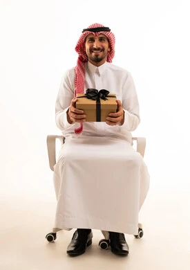 رجل سعودي مبتسم يحمل صندوق هدايا بخلفية بيضاء