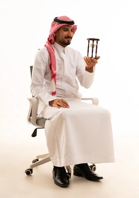 رجل أعمال سعودي يحمل ساعة رملية بخلفية بيضاء