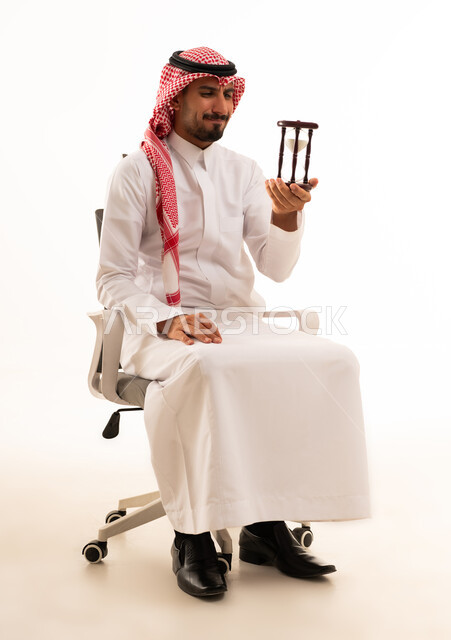 رجل أعمال سعودي يمسك ساعة رملية في المكتب