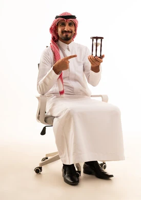 رجل سعودي يحمل ساعة رملية على كرسي مكتب