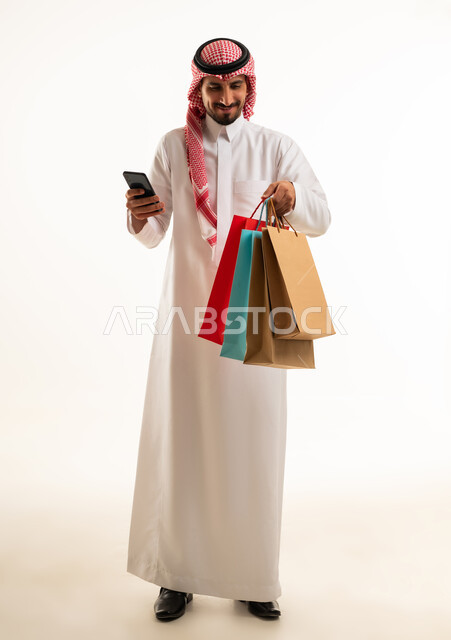 رجل سعودي مع أكياس تسوق وهاتف ذكي