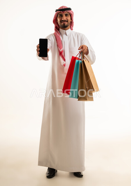 رجل سعودي يحمل حقائب تسوق وشاشة هاتف