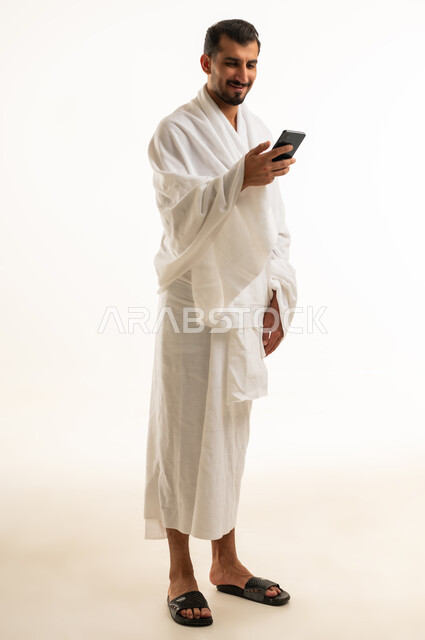 Saudi Pilgrim in Ihram Using Smartphone on White Background