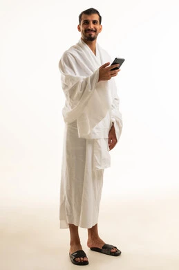 رجل سعودي بملابس الإحرام يمسك هاتفاً ذكياً بخلفية بيضاء
