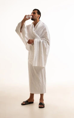 رجل سعودي بملابس الإحرام يشرب الماء بخلفية بيضاء رجل سعودي بملابس الإحرام يشرب الماء بخلفية بيضاء