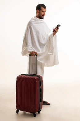 رجل سعودي بملابس الإحرام مع حقيبة سفر وهاتف