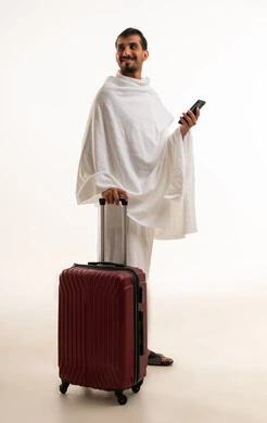 رجل سعودي بملابس الإحرام مع حقيبة سفر وجوال
