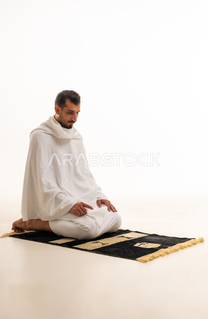 رجل سعودي بملابس الإحرام يصلي على خلفية بيضاء