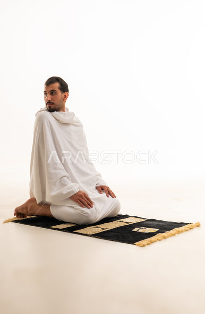 رجل مسلم بملابس الإحرام يؤدي الصلاة بخلفية بيضاء