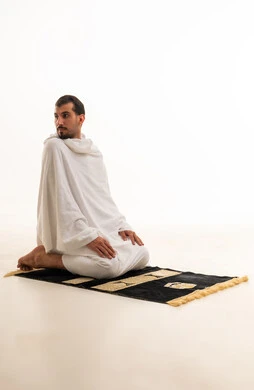 رجل مسلم بملابس الإحرام يؤدي الصلاة بخلفية بيضاء