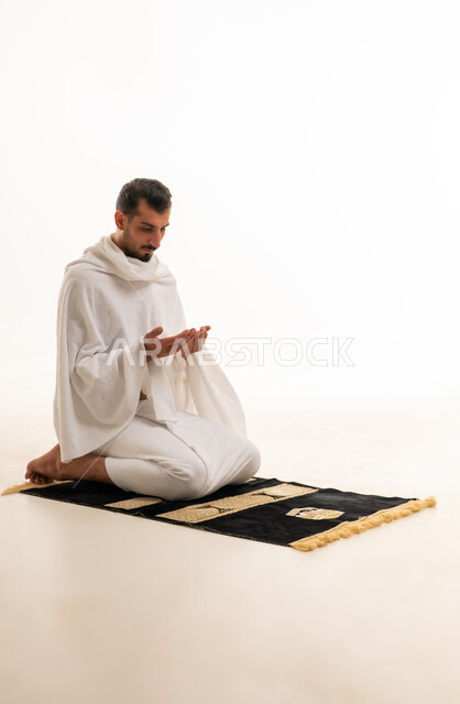 رجل سعودي بملابس الإحرام يدعو على خلفية بيضاء