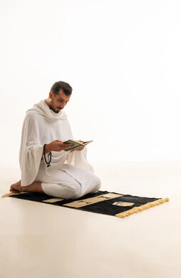 رجل مسلم بملابس الإحرام يقرأ القرآن على سجادة الصلاة