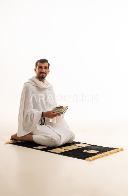 رجل سعودي بملابس الإحرام يحمل المصحف على سجادة الصلاة