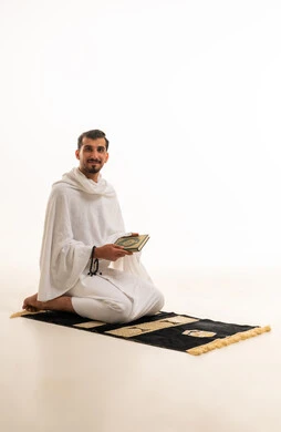 رجل سعودي بملابس الإحرام يحمل المصحف على سجادة الصلاة