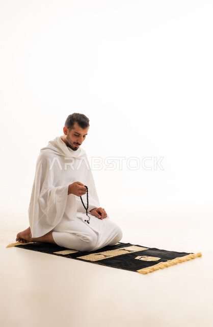 رجل سعودي بملابس الإحرام يمسك سبحة على خلفية بيضاء