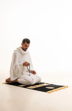 رجل سعودي بملابس الإحرام يمسك سبحة على خلفية بيضاء