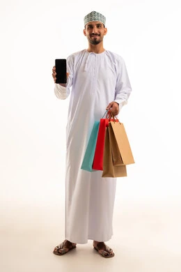رجل عُماني يحمل هاتفاً ذكياً وأكياس تسوق