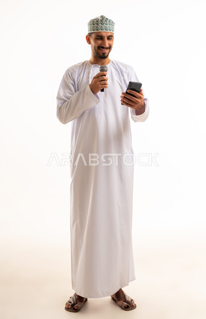 رجل عماني يمسك ميكروفون وهاتف ذكي خلفية بيضاء