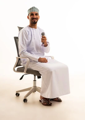 رجل عُماني يمسك ميكروفون ويجلس على كرسي مكتب