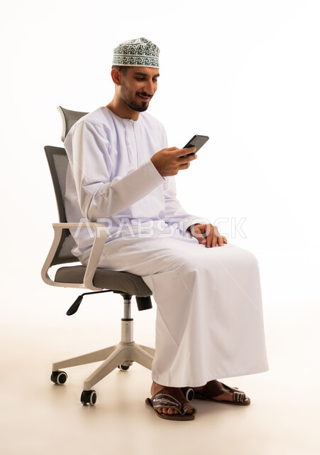 رجل عماني يرتدي الزي التقليدي يستخدم الهاتف الذكي