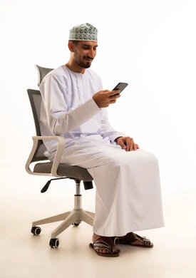 Omani Man in Traditional Dress Using Smartphone on Chair
