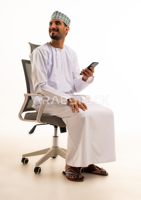 رجل عماني مع هاتف ذكي يجلس على كرسي مكتب