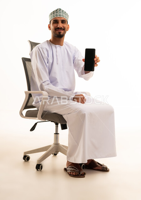 رجل عُماني يحمل هاتفاً ذكياً على كرسي مكتب