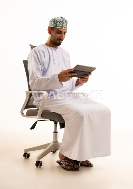 رجل عماني بالزي التقليدي يستخدم جهاز لوحي في المكتب