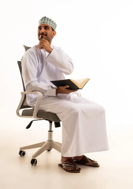 رجل عماني بالزي التقليدي يقرأ على كرسي مكتب