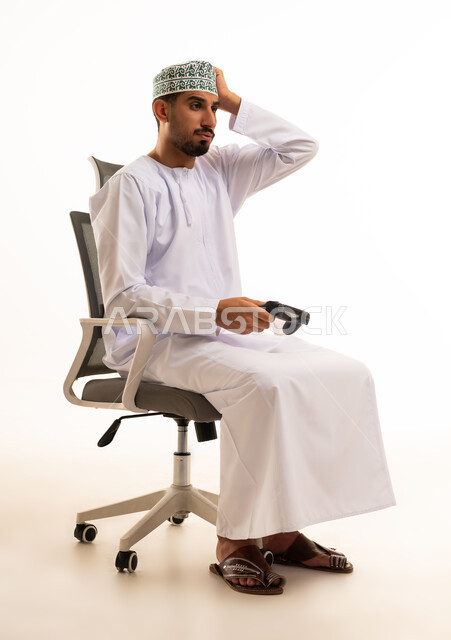 رجل عُماني مع جهاز تحكم ألعاب على خلفية بيضاء