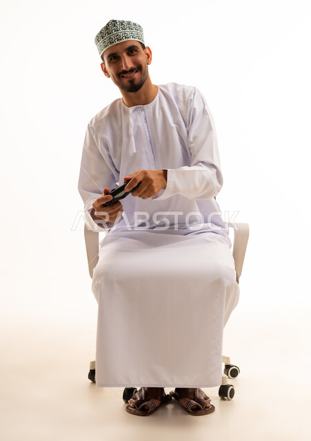 رجل عماني بالزي التقليدي يمسك بجهاز تحكم الألعاب