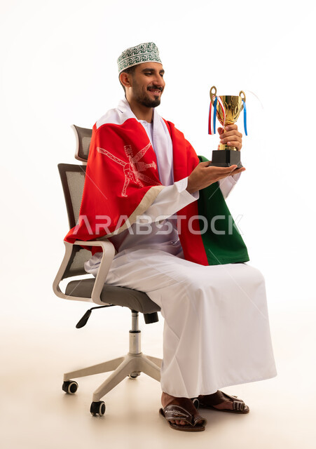 رجل عماني يحمل كأس الفوز مع علم السلطنة