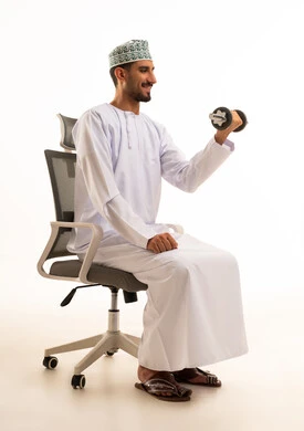 رجل عماني يمارس الرياضة بالدامبل على كرسي مكتب