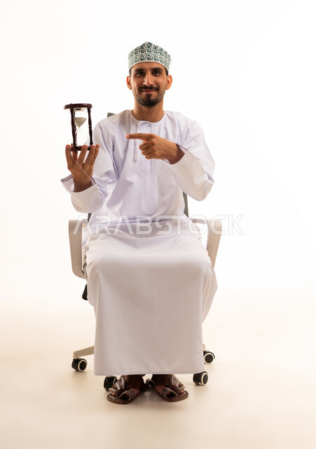 رجل عماني يحمل ساعة رملية على كرسي مكتب