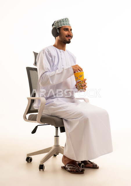 رجل عماني يرتدي سماعات وممسك بالفشار في كرسي مكتب