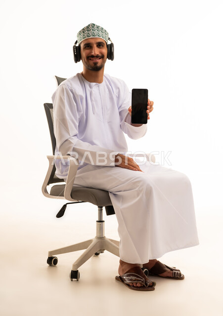 رجل عماني يرتدي سماعات ويحمل هاتفا ذكيا