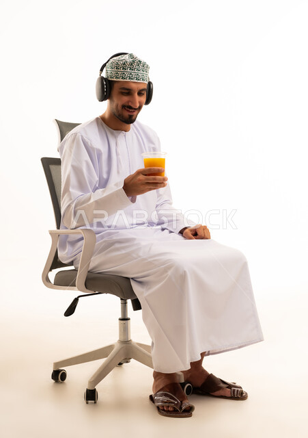 Omani Man with Headphones Drinking Juice in Office Chair