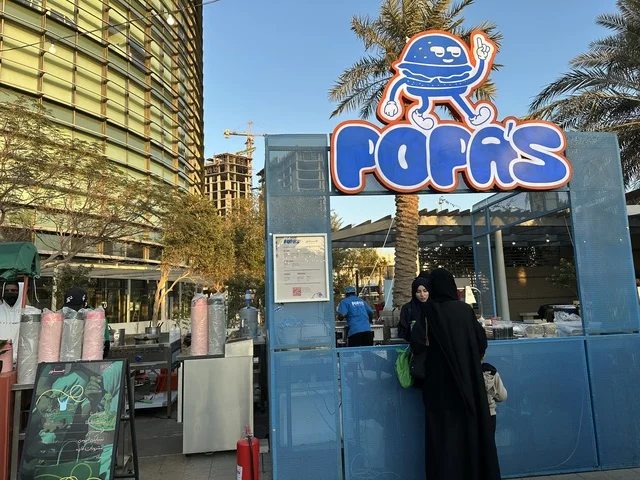 Visitors gathered at the Jood Market in Prince Saud Park in Dhahran, Eastern Province, Saudi Arabia. It is an open community market that supports local projects, featuring artisanal products and homemade foods, outdoor shopping areas, family events, and recreational activities, all set in a vibrant heritage and social atmosphere.
