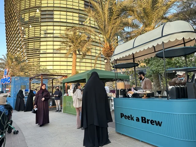 تجمع الزوار في سوق جذور في حديقة الأمير سعود بمدينة الظهران، المنطقة الشرقية، المملكة العربية السعودية، سوق مجتمعي مفتوح يدعم المشاريع المحلية، منتجات حرفية وأطعمة منزلية، أركان تسوق خارجية ، فعاليات عائلية وأنشطة ترفيهية، أجواء تراثية واجتماعية نابضة بالحياة