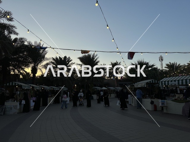 Visitors gathered at the Jood Market in Prince Saud Park in Dhahran, Eastern Province, Saudi Arabia. It is an open community market that supports local projects, featuring artisanal products and homemade foods, outdoor shopping areas, family events, and recreational activities, all set in a vibrant heritage and social atmosphere.